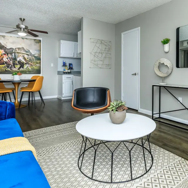 A modern living room featuring a blue sofa, a circular coffee table, and a dining area with orange chairs.