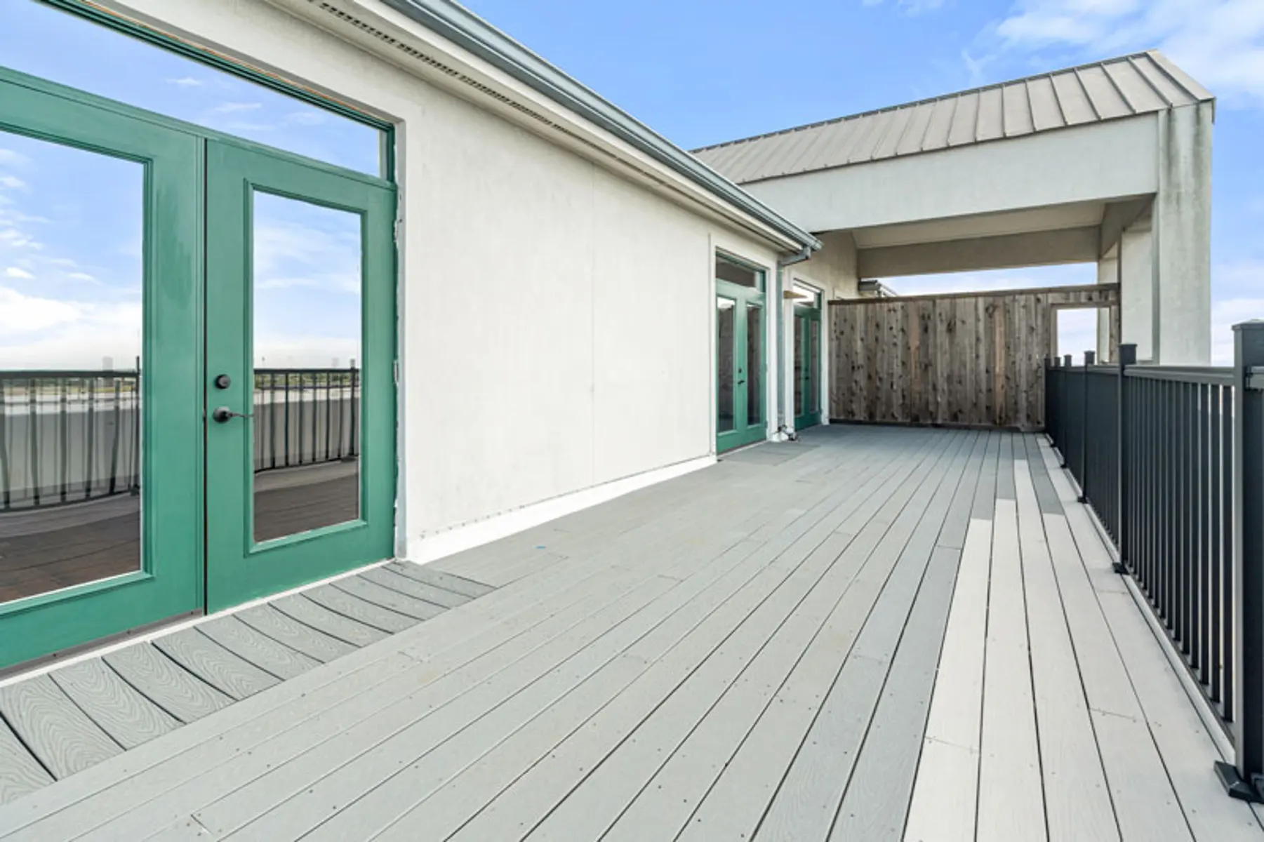 A spacious rooftop terrace with wooden flooring and green doors leading to an interior space.