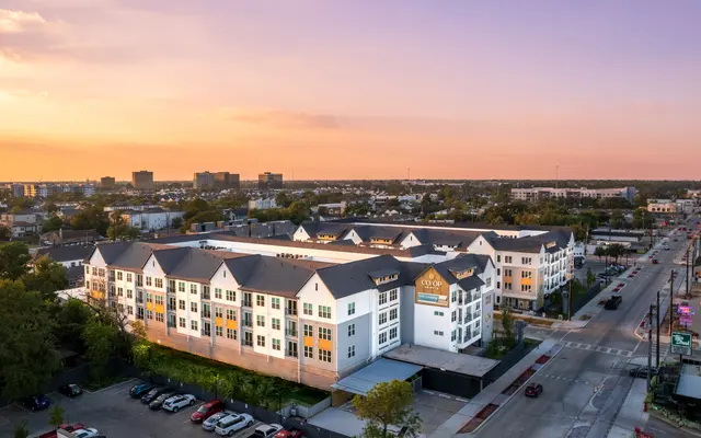 Aerial view of a modern apartment complex during sunset, with surrounding roads and vehicles visible.