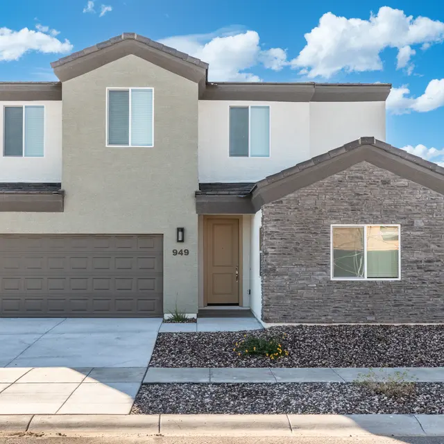A modern two-story house with a beige and stone exterior, featuring a two-car garage, large windows, and a well-maintained front yard with gravel landscaping.