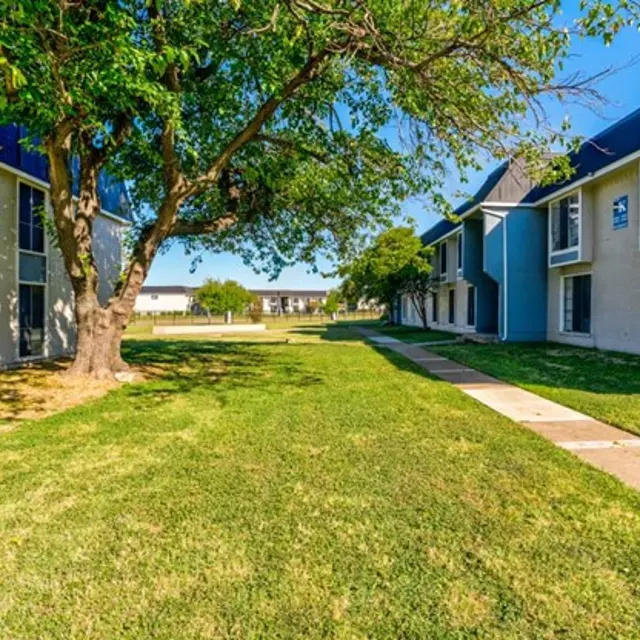 A view of a spacious apartment complex with two buildings flanking a green lawn and pathway.