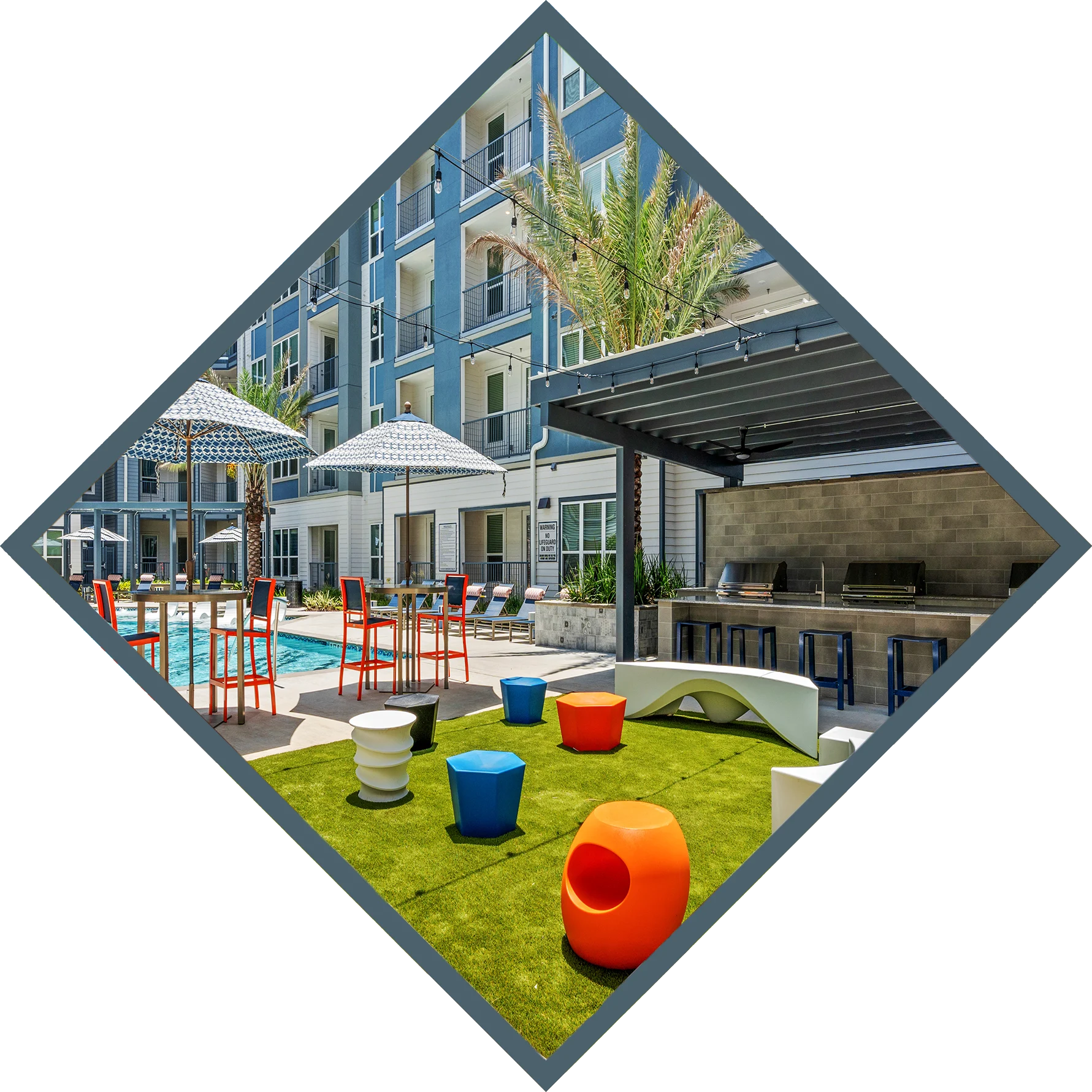 A modern apartment complex outdoor pool area featuring colorful lounge chairs, umbrellas, and vibrant stools on green grass.