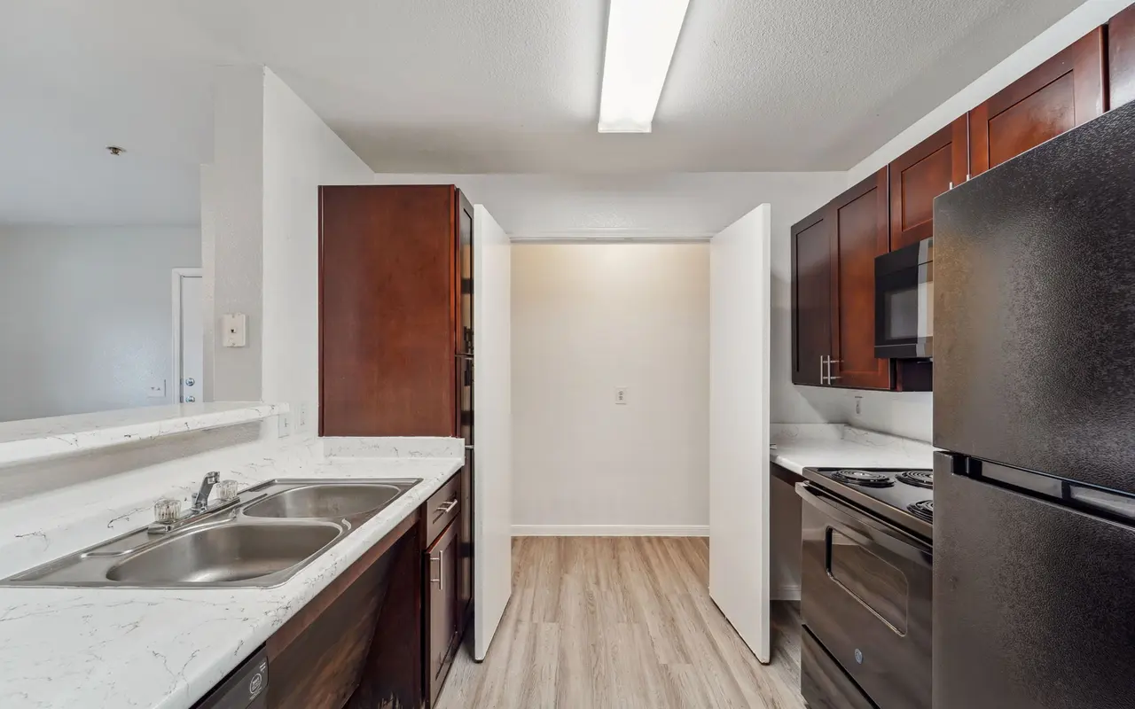 A modern kitchen featuring dark wood cabinetry, stainless steel appliances, and a double sink with a marble countertop.