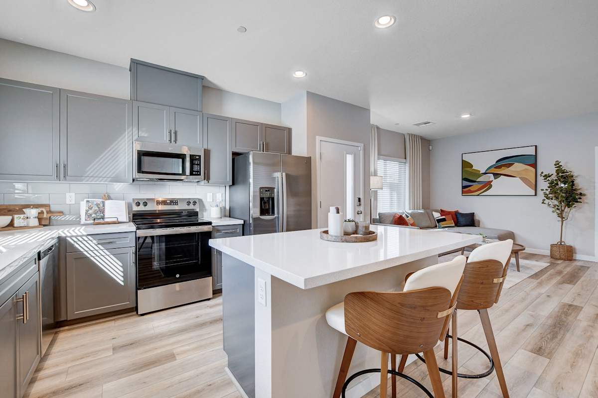 Stylish Modern Kitchen and Living Area A modern kitchen with gray cabinets and a white countertop, featuring bar stools and an open layout to a cozy living area with natural light.