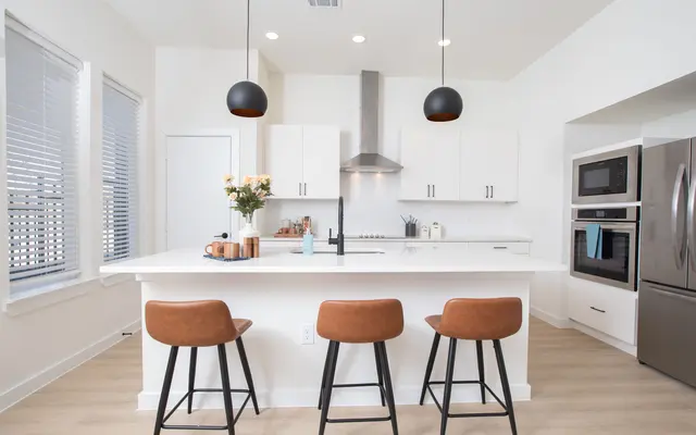 Contemporary Kitchen Design A modern kitchen featuring a central island with bar stools, white cabinetry, stainless steel appliances, and large windows with blinds allowing natural light.