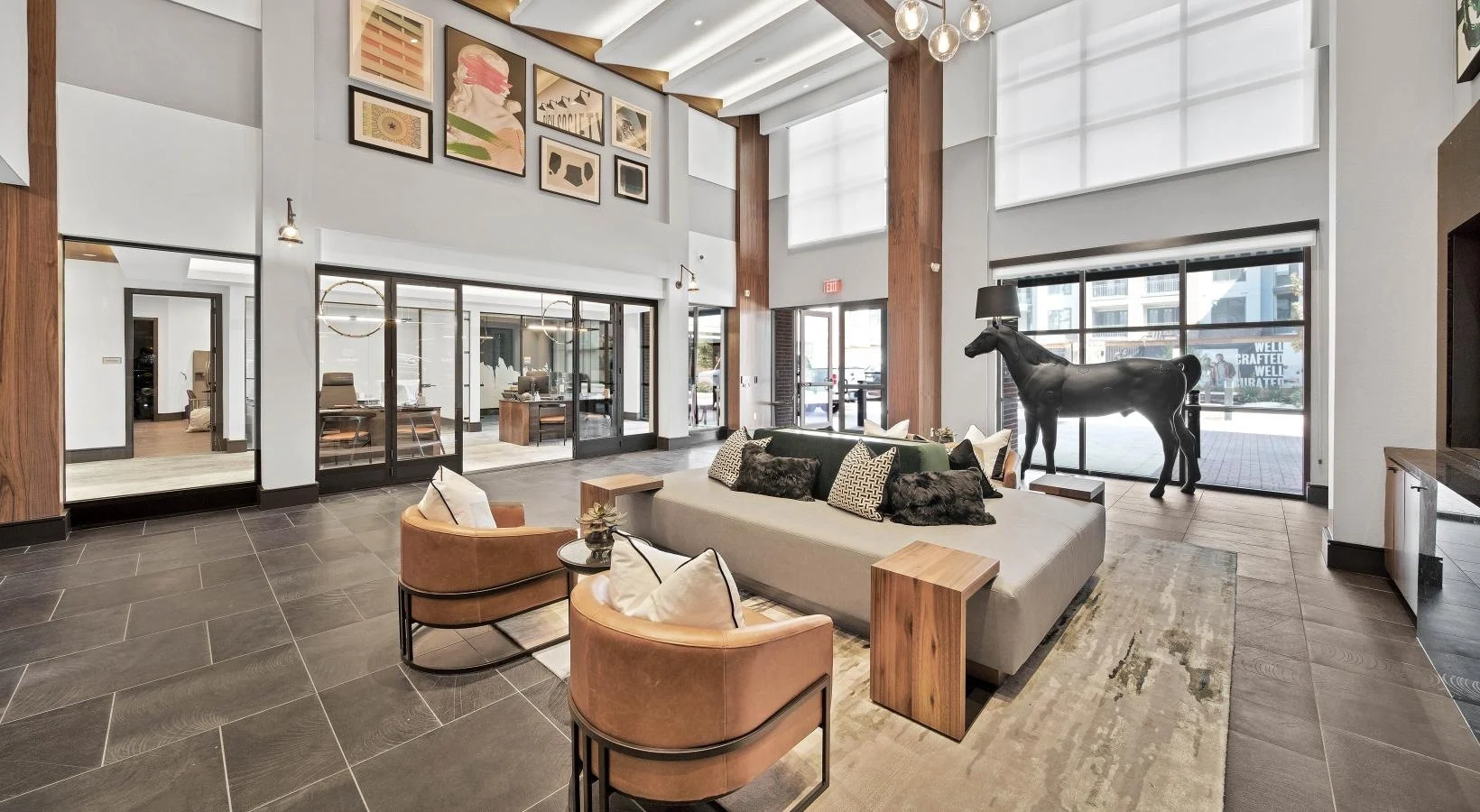 A modern lobby featuring a mix of contemporary and rustic design elements, with a gray couch, brown accent chairs, and a horse sculpture.