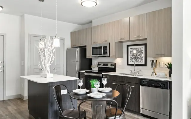 Modern kitchen with stainless steel appliances, an island, and a dining table set for two, featuring minimalist decor.