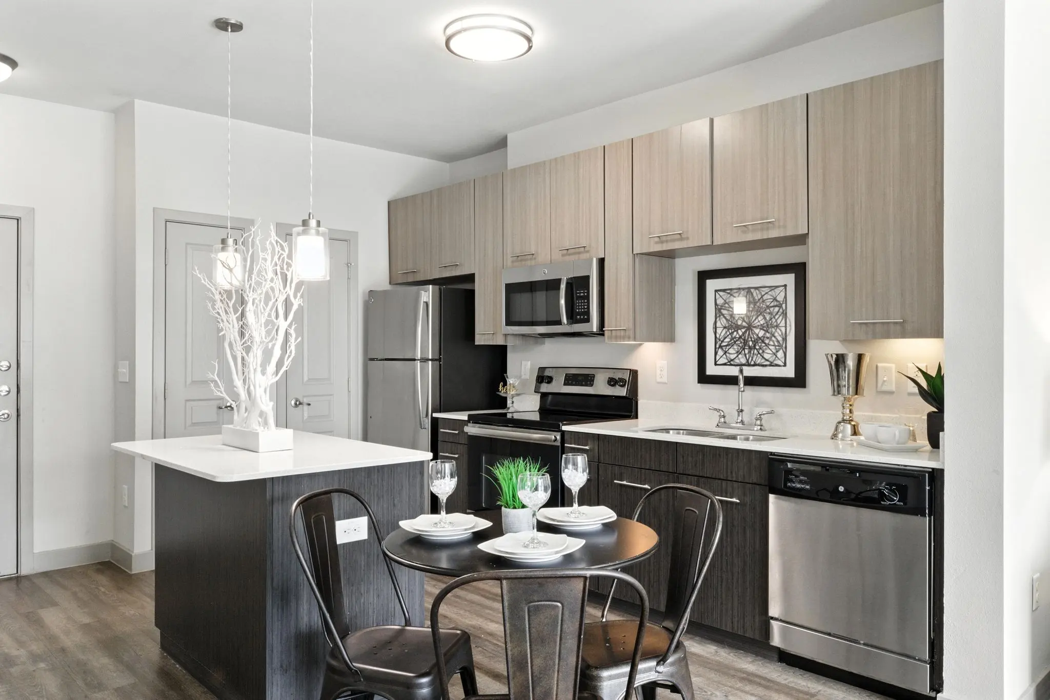 Modern kitchen with stainless steel appliances, an island, and a dining table set for two, featuring minimalist decor.