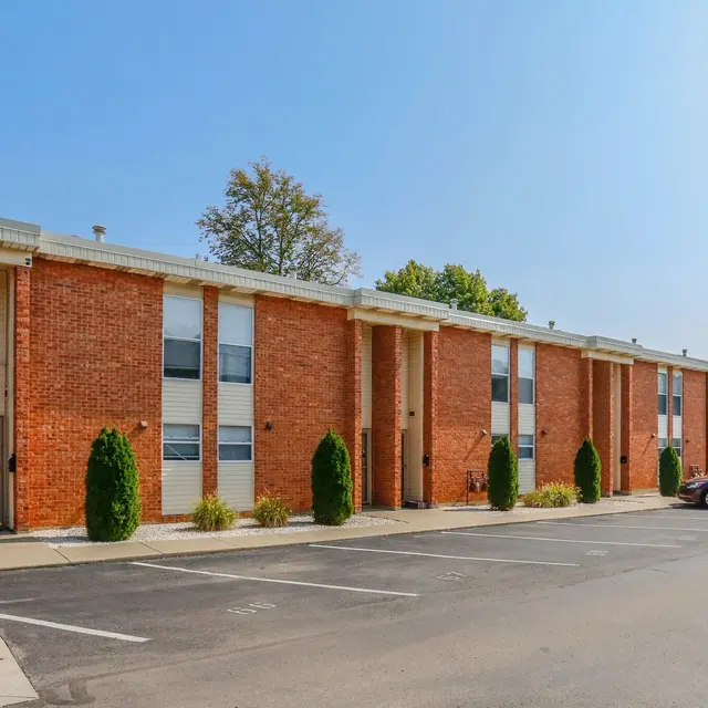Exterior view of a brick apartment building with trees in the background and parked cars in the foreground.