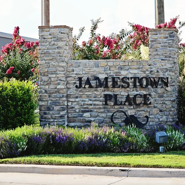 A stone sign displaying 'JAMESTOWN PLACE' surrounded by colorful flowers and greenery.
