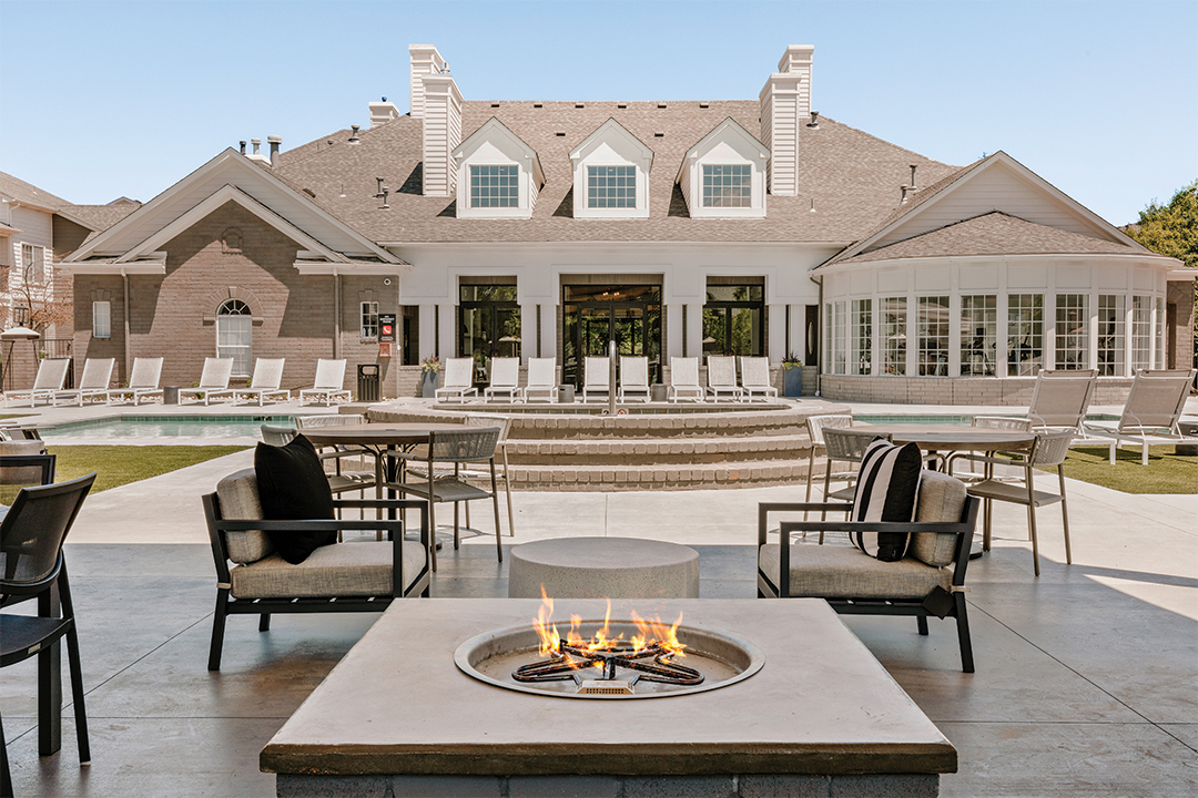 Outdoor Poolside Recreation Area Outdoor recreational area featuring a fire pit surrounded by chairs, leading to a building with large windows and lounge chairs by the pool.