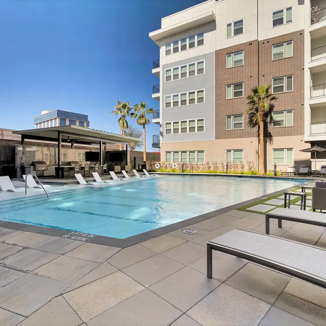 A modern apartment complex pool area with lounge chairs and palm trees.