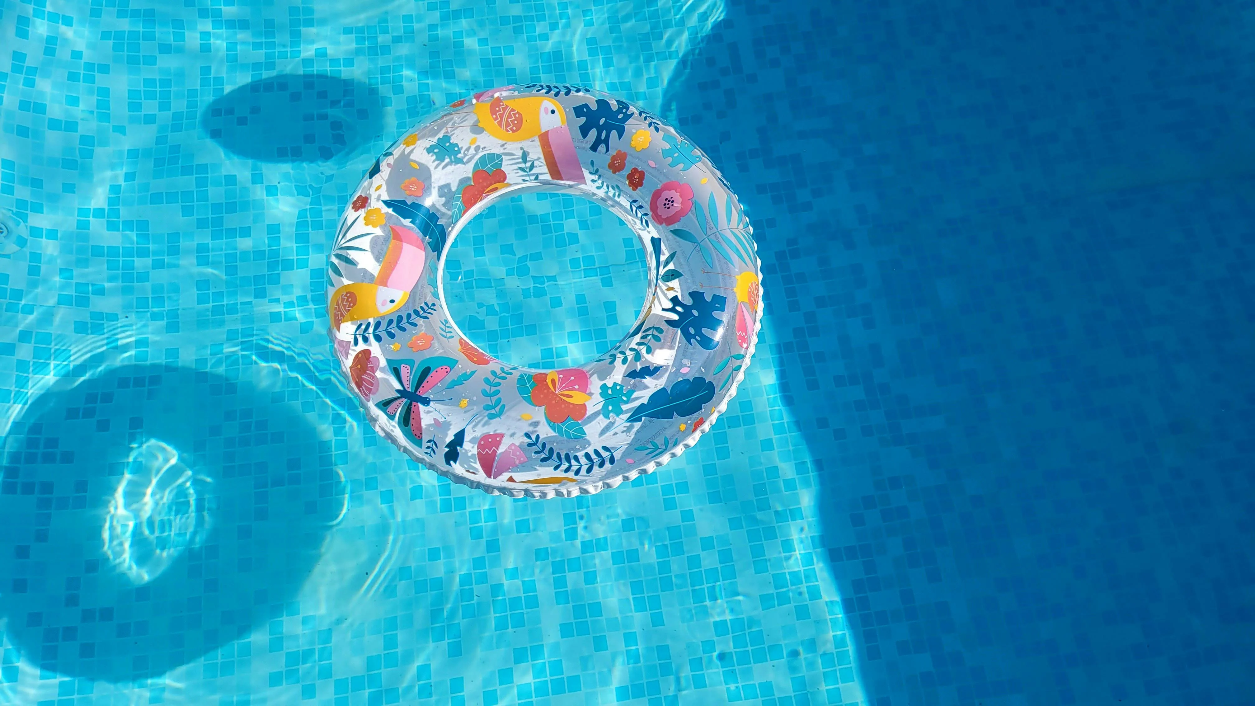 A colorful inflatable pool float with floral patterns floating on blue water.