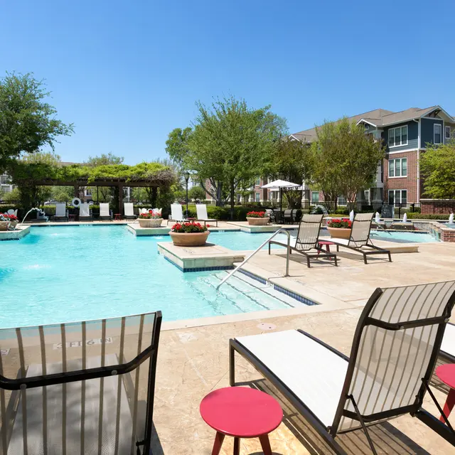 View of a pool area with lounge chairs, umbrellas, and landscaping