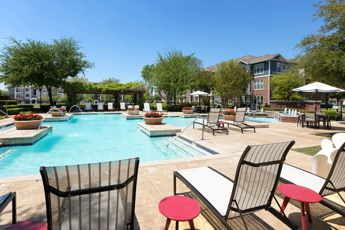 View of a pool area with lounge chairs, umbrellas, and landscaping