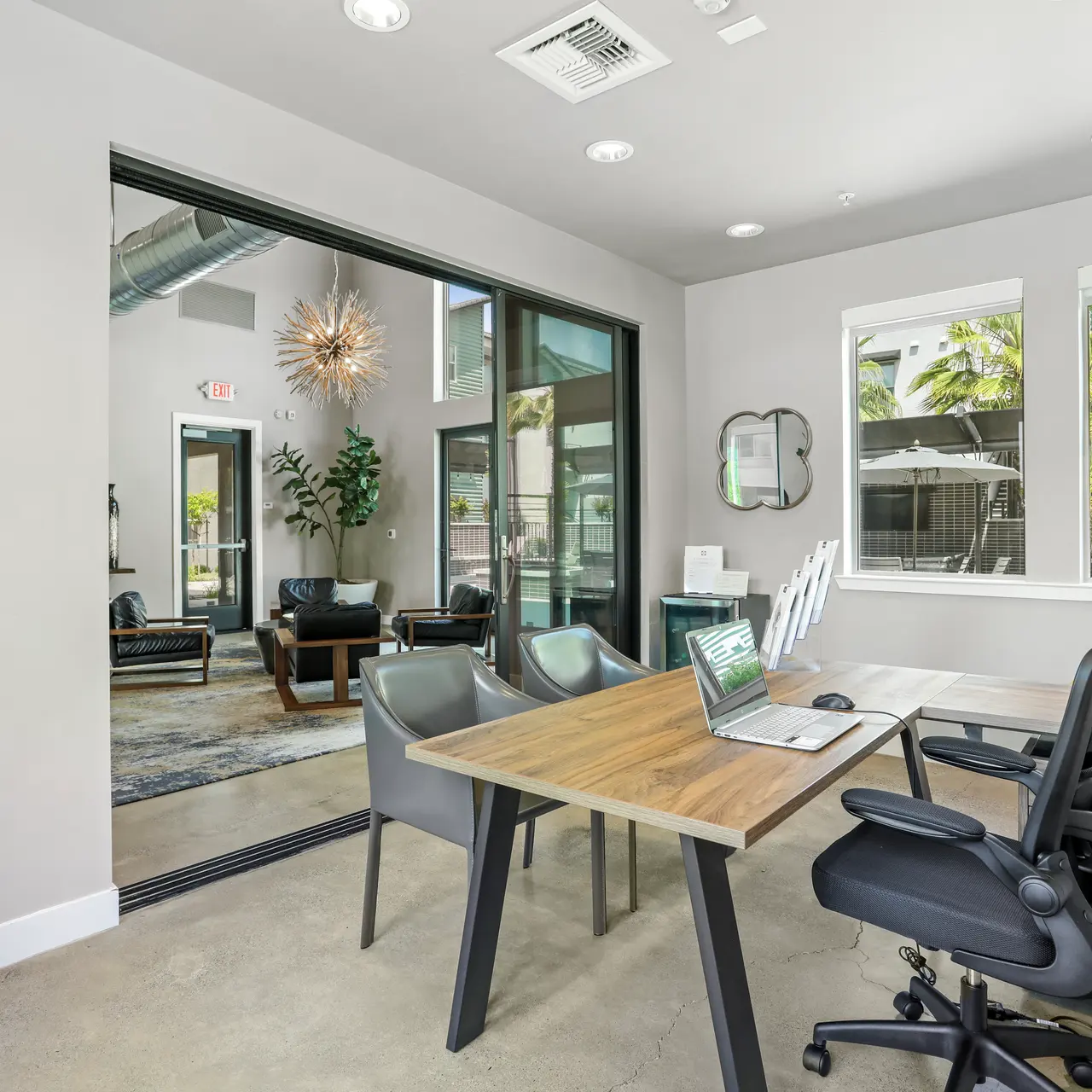 A modern office with a sleek desk, ergonomic chairs, and large windows allowing natural light. The space features contemporary decor and a view into a lounge area with comfortable seating.