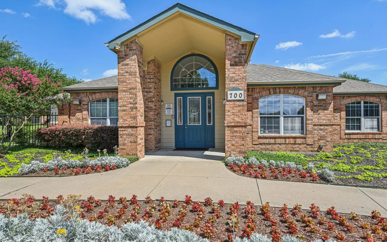A brick building with a blue door, surrounded by landscaped flowers and plants, under a clear blue sky.