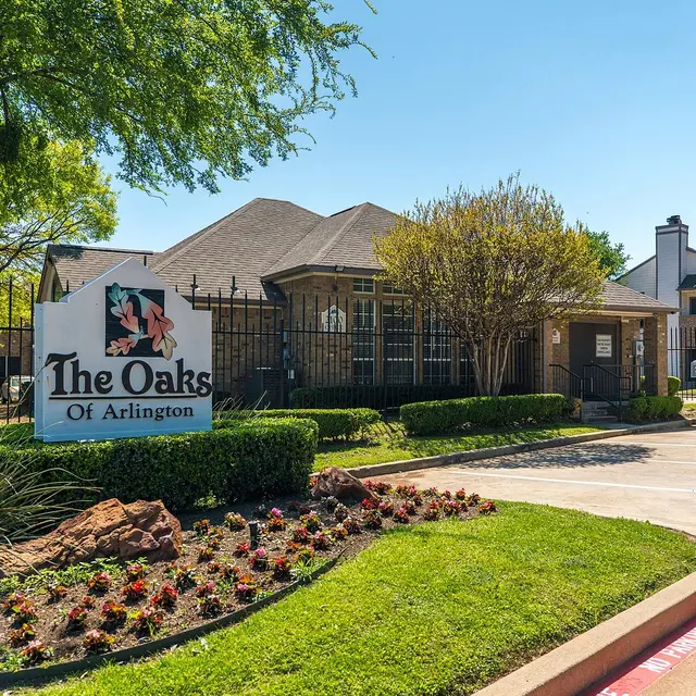 Facade of The Oaks of Arlington, a residential community, with a decorative sign and well-maintained landscaping.