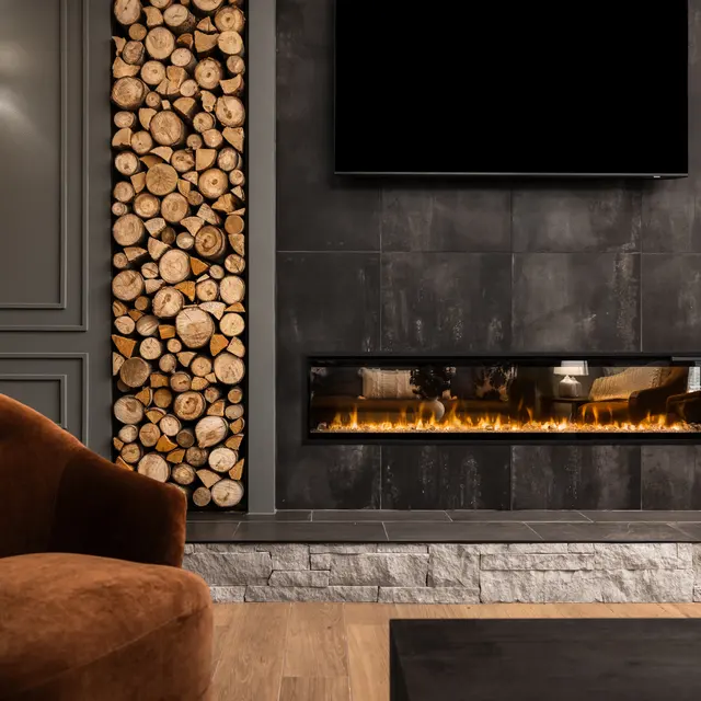 A stylish living room featuring a wall with neatly stacked logs on either side of a modern fireplace. The fireplace has a sleek design, with a flat screen TV mounted above it. The space is complemented by an elegant brown armchair and a dark coffee table on a wooden floor.