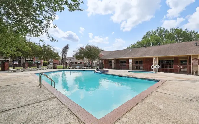 Swimming Pool Area in Apartment Complex A swimming pool in an apartment complex surrounded by lounge chairs and trees, under a partly cloudy sky.