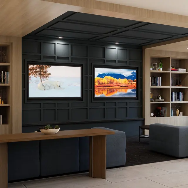 A modern living space featuring two sofas, two large screens displaying nature scenes, and bookshelves filled with books and decor items.
