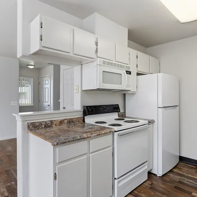 Modern Apartment Kitchen A modern kitchen in an apartment space featuring white cabinetry, a black stove, a microwave, and a refrigerator. The kitchen has a small breakfast bar and wooden flooring.