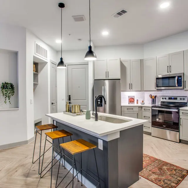A modern kitchen featuring gray cabinets, stainless steel appliances, and a center island with bar stools.