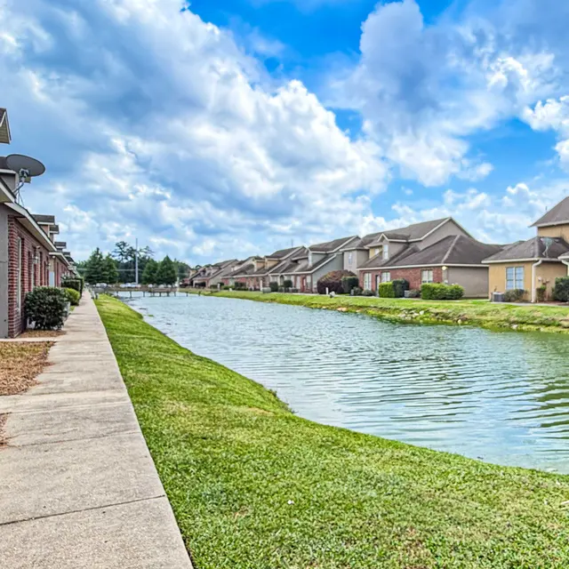 A peaceful waterfront view with a walking path beside a calm canal, flanked by residential buildings on either side.