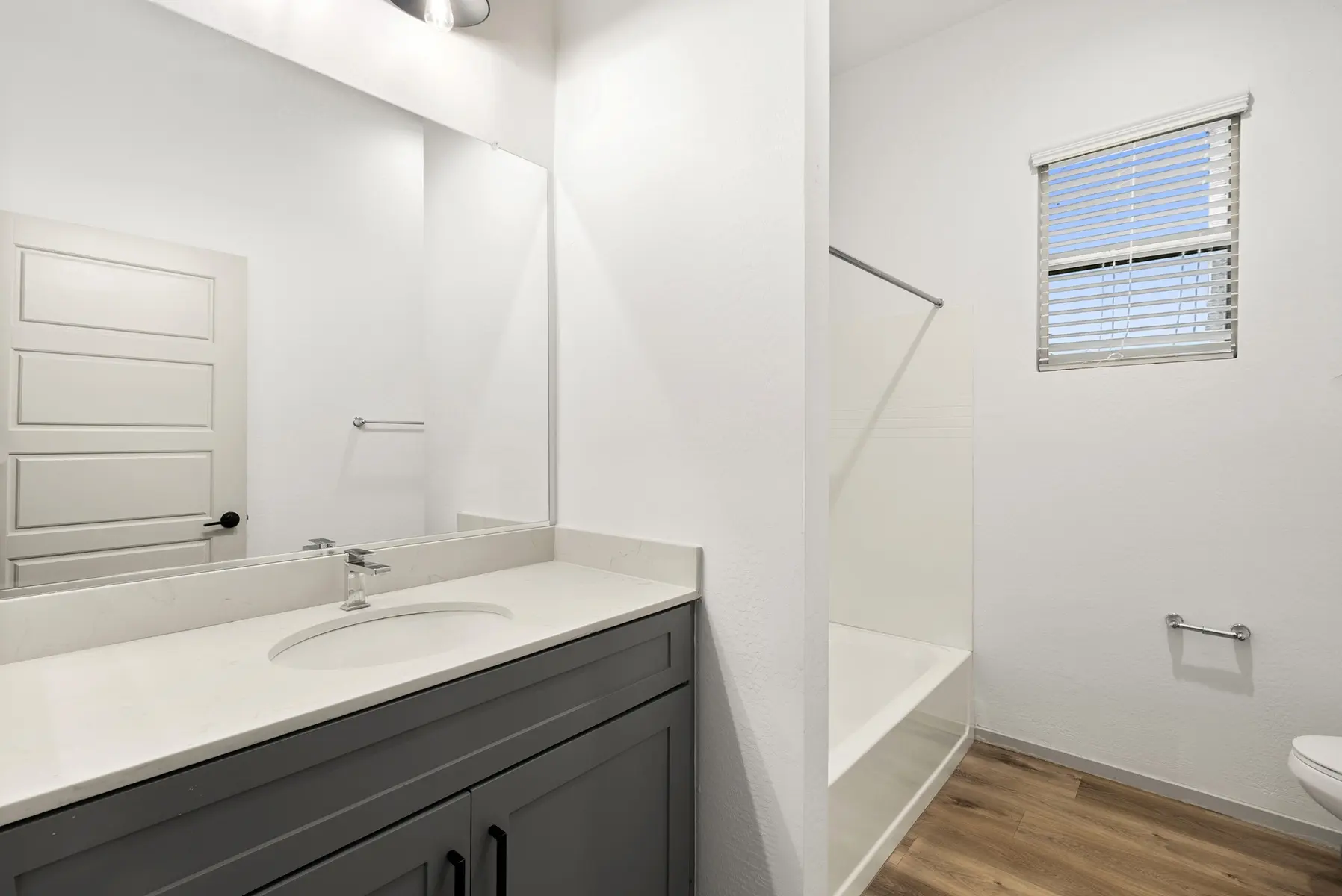Modern bathroom featuring a double sink vanity, a walk-in shower, and natural light from a window, with light wood flooring.
