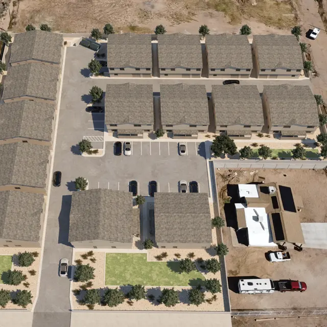 Aerial view of a residential complex featuring several buildings, parking spaces, and landscaping areas with trees.