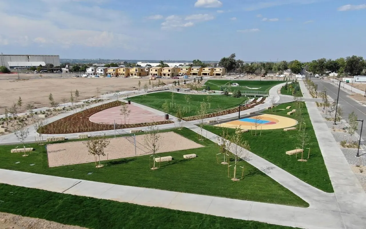 An aerial view of a modern park featuring green lawns, walking paths, and recreational zones with play areas and benches.