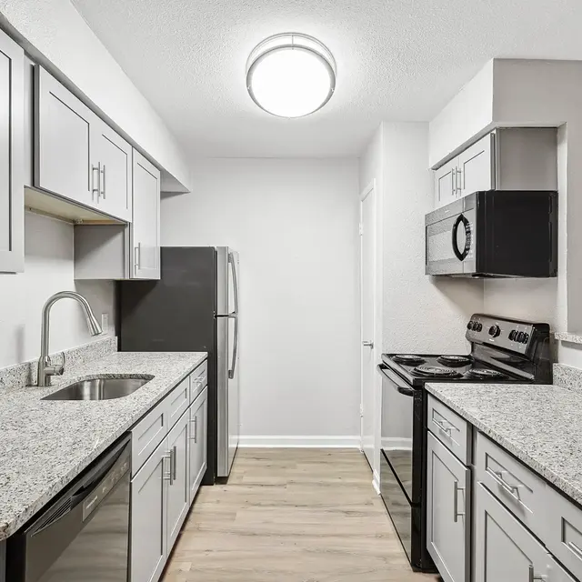 A modern kitchen featuring gray cabinets, stainless steel appliances, and granite countertops with a focus on clean lines and a bright atmosphere.