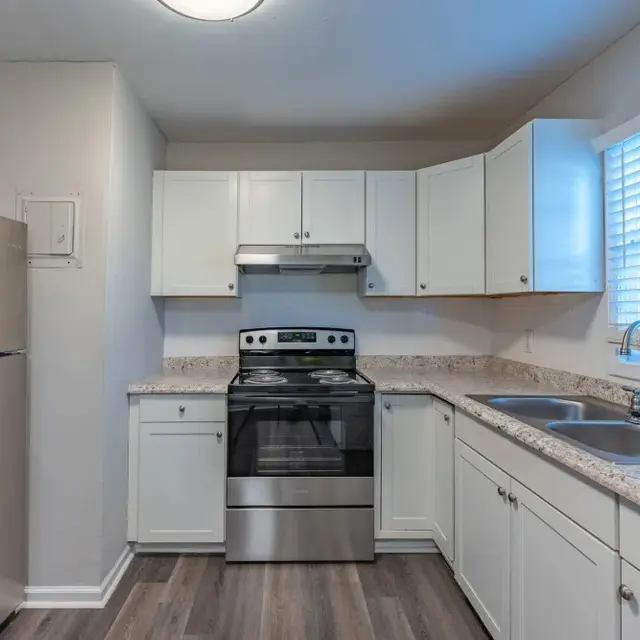 A modern kitchen featuring a stainless steel refrigerator, an oven with a stove, and a double sink. White cabinetry and granite countertops provide a clean and bright look, with a window letting in natural light.