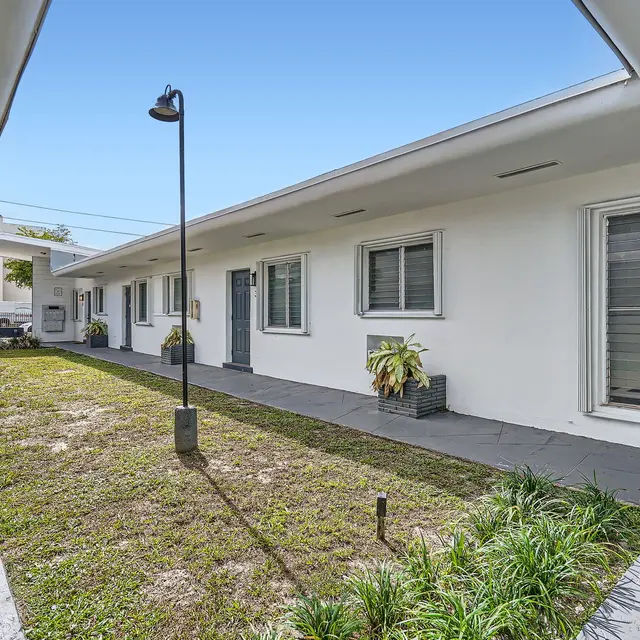 A view of a modern apartment courtyard with a grass patch and pathways surrounded by white buildings.