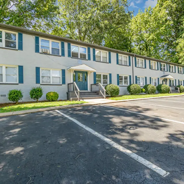 A multi-unit apartment building surrounded by greenery and parking spaces.