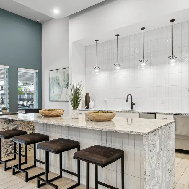 EKOS Lake Shadow A modern kitchen with a white marble island, black stools, and stylish lighting fixtures against a blue wall.