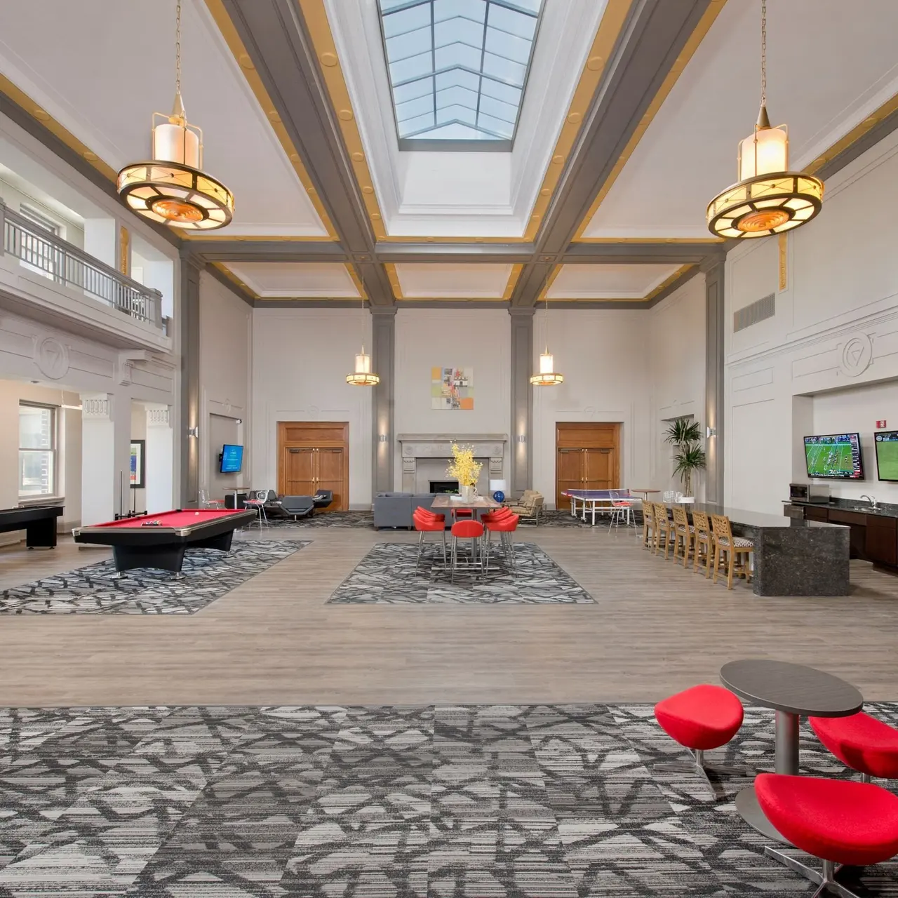 Spacious lobby with high ceilings, elegant lighting, and modern furnishings, featuring a pool table, seating areas, and televisions.