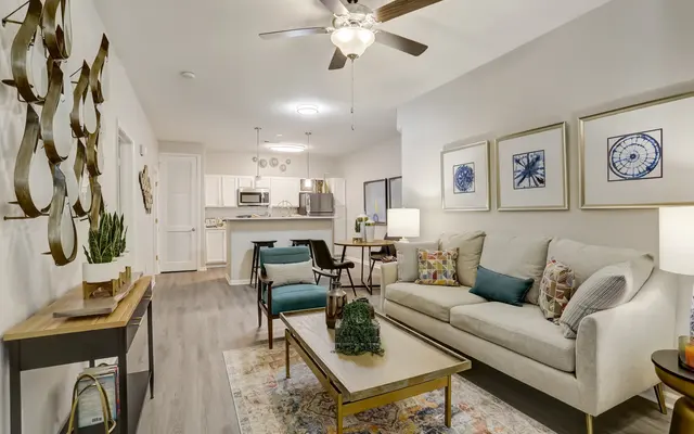 A stylish living room featuring a light-colored sofa, decorative pillows, a coffee table, and a rug, with a dining area visible in the background.