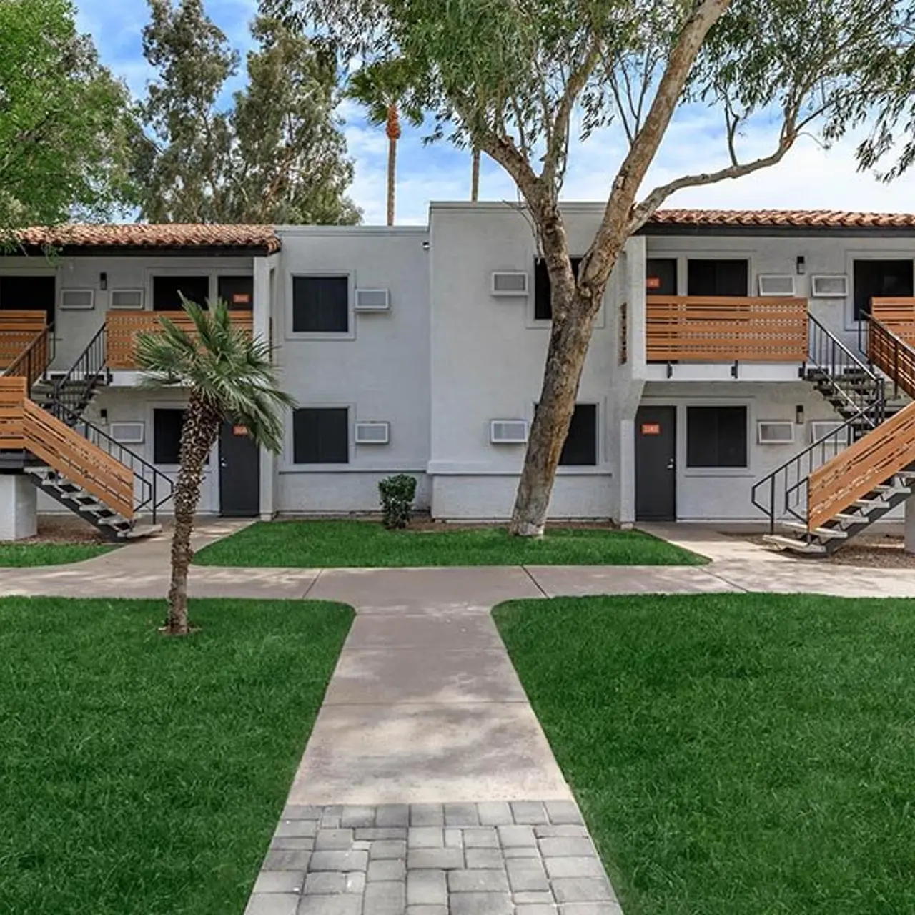 Exterior view of a two-story apartment building with wooden staircases and green lawn in the foreground.