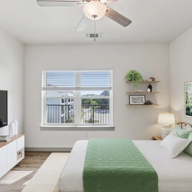 A modern bedroom featuring a queen-size bed with a green throw blanket, a wall-mounted TV, and decorative elements like shelves and framed artwork.