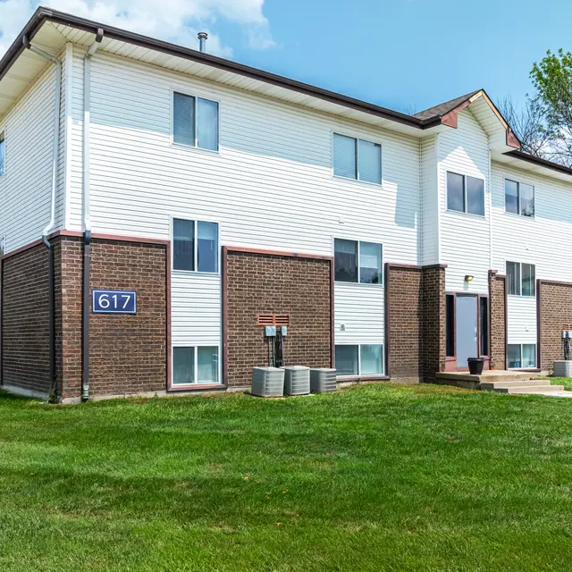 Apartment Building 617 Exterior Exterior view of a two-story apartment building with the number 617 visible, featuring a mix of white siding and brown brick, surrounded by a grassy area and trees.