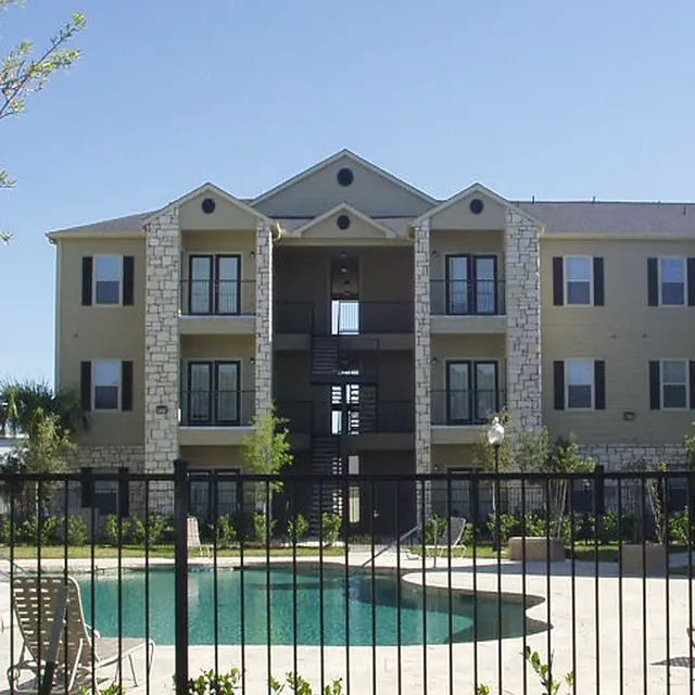 A view of a modern apartment complex with a swimming pool and landscaped area in the foreground.