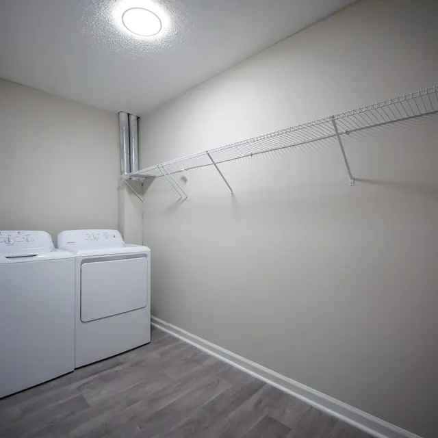A small laundry room featuring a washer and dryer side by side, with a wire shelf mounted above them.