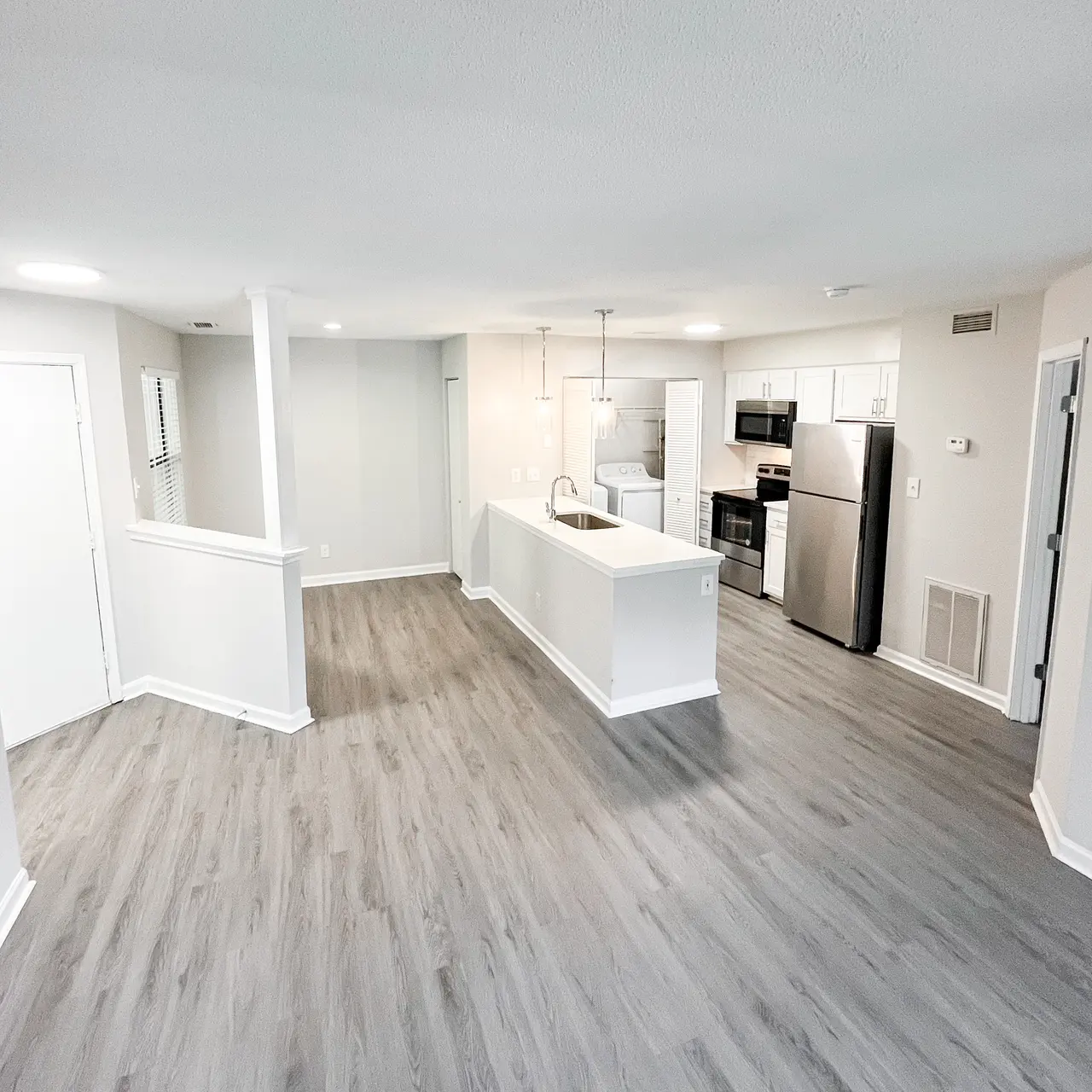 Spacious Modern Apartment Interior A spacious modern apartment with a light grey floor, an open layout including a kitchen with stainless steel appliances, a white island, and natural light coming from several windows.