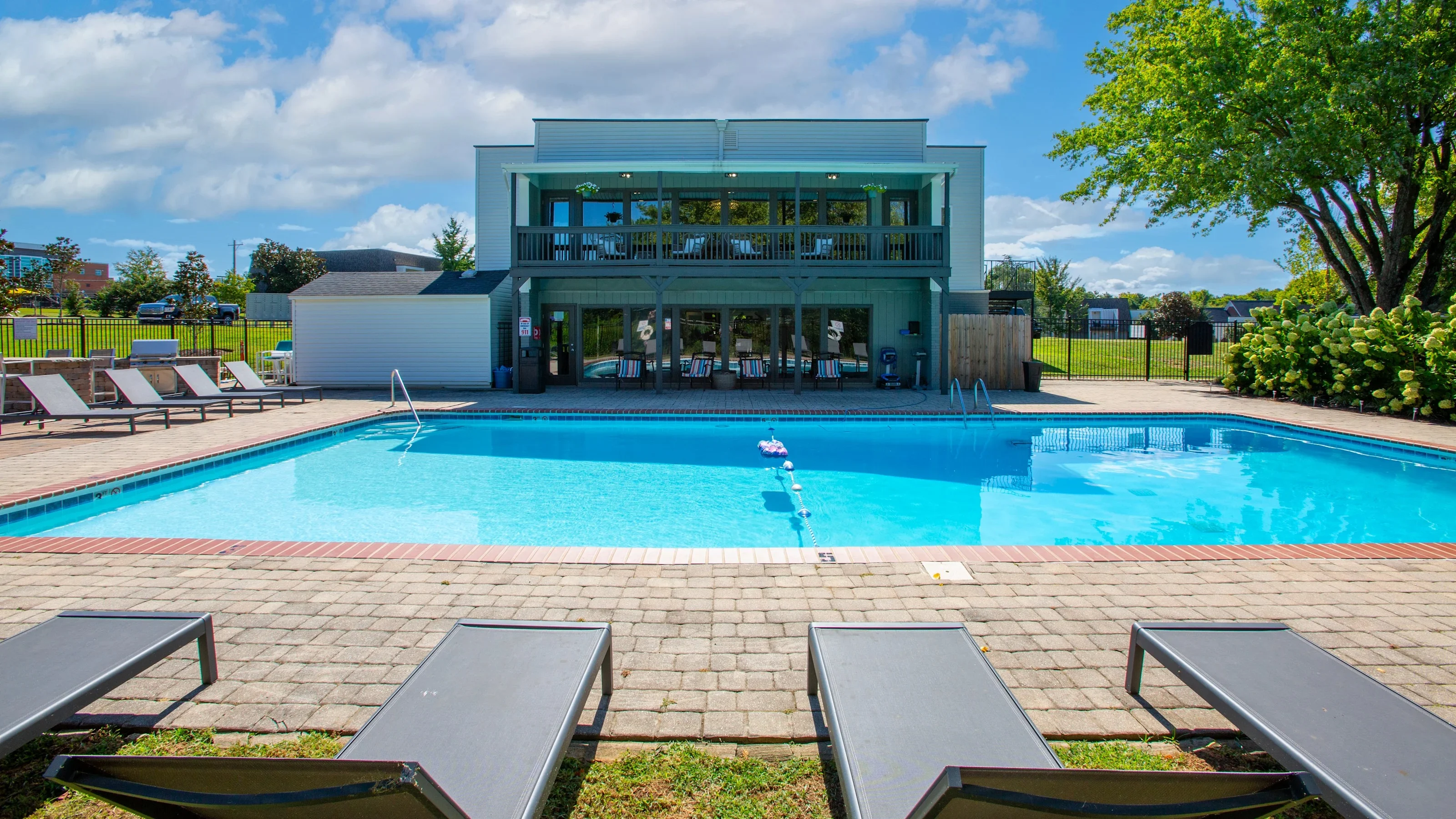 Modern Swimming Pool Area A view of a swimming pool area featuring lounge chairs and a modern building in the background under a partly cloudy sky.