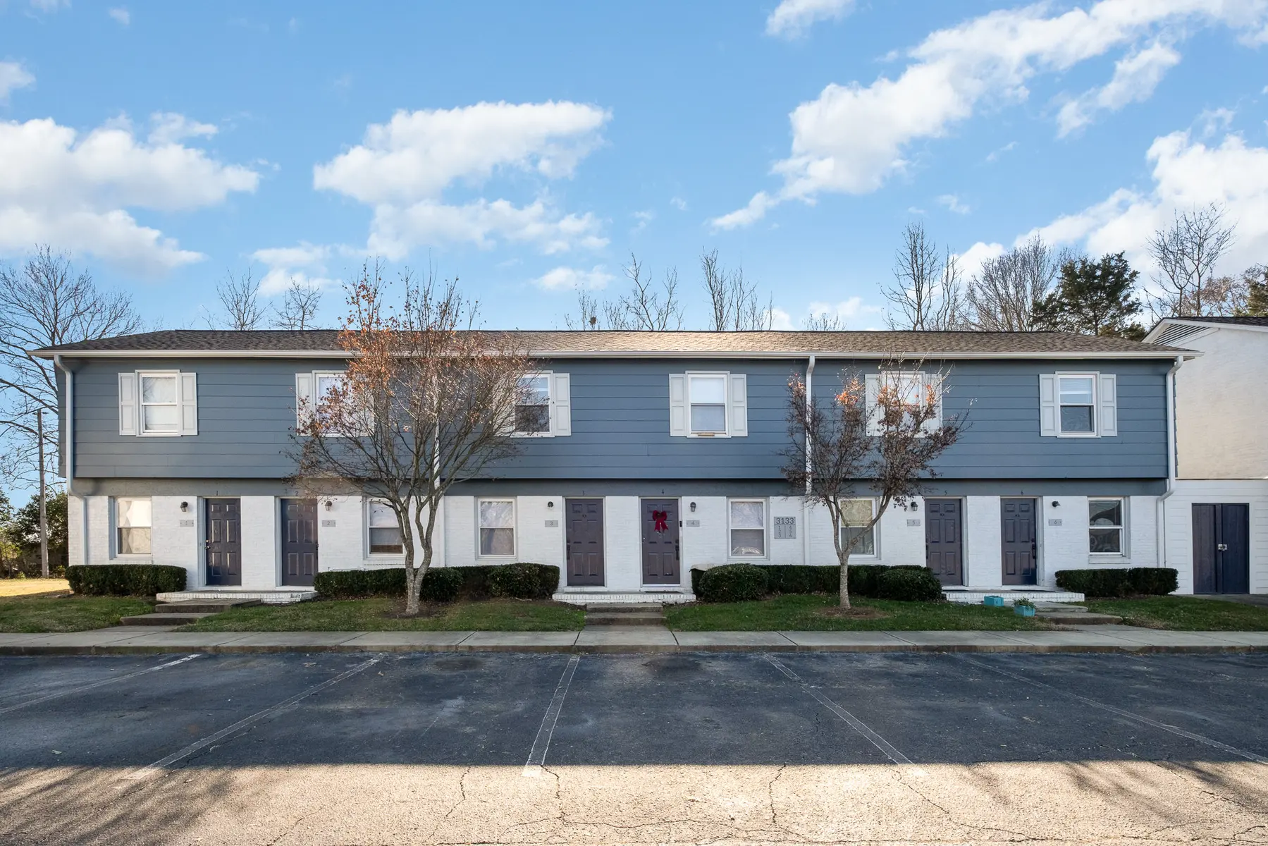 A row of townhouses with a blue exterior, featuring trees in front and a cloudy sky overhead.