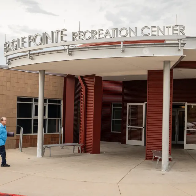 Eagle Pointe Recreation Center Entrance A man walking towards the entrance of the Eagle Pointe Recreation Center, which features a modern, red and tan exterior and large signage.