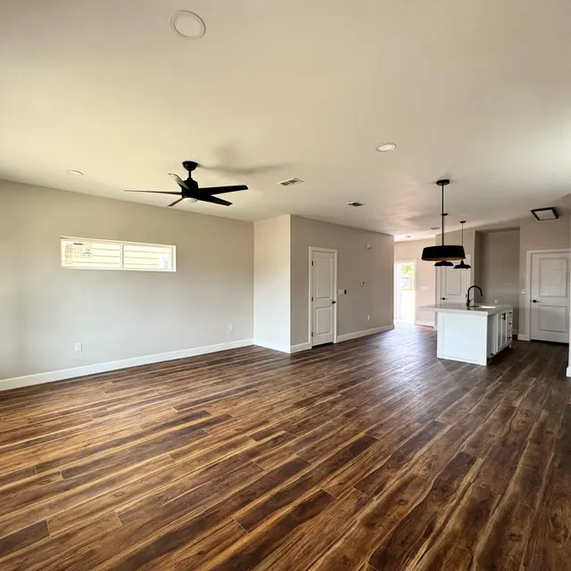 A spacious living room featuring hardwood floors, a ceiling fan, and open layout towards a kitchen area.