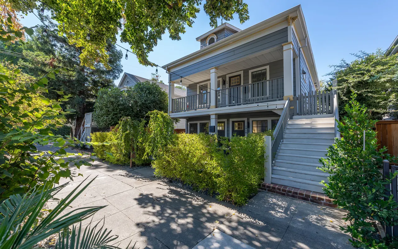 A charming two-story house with a wide staircase and a large front porch, surrounded by lush greenery.