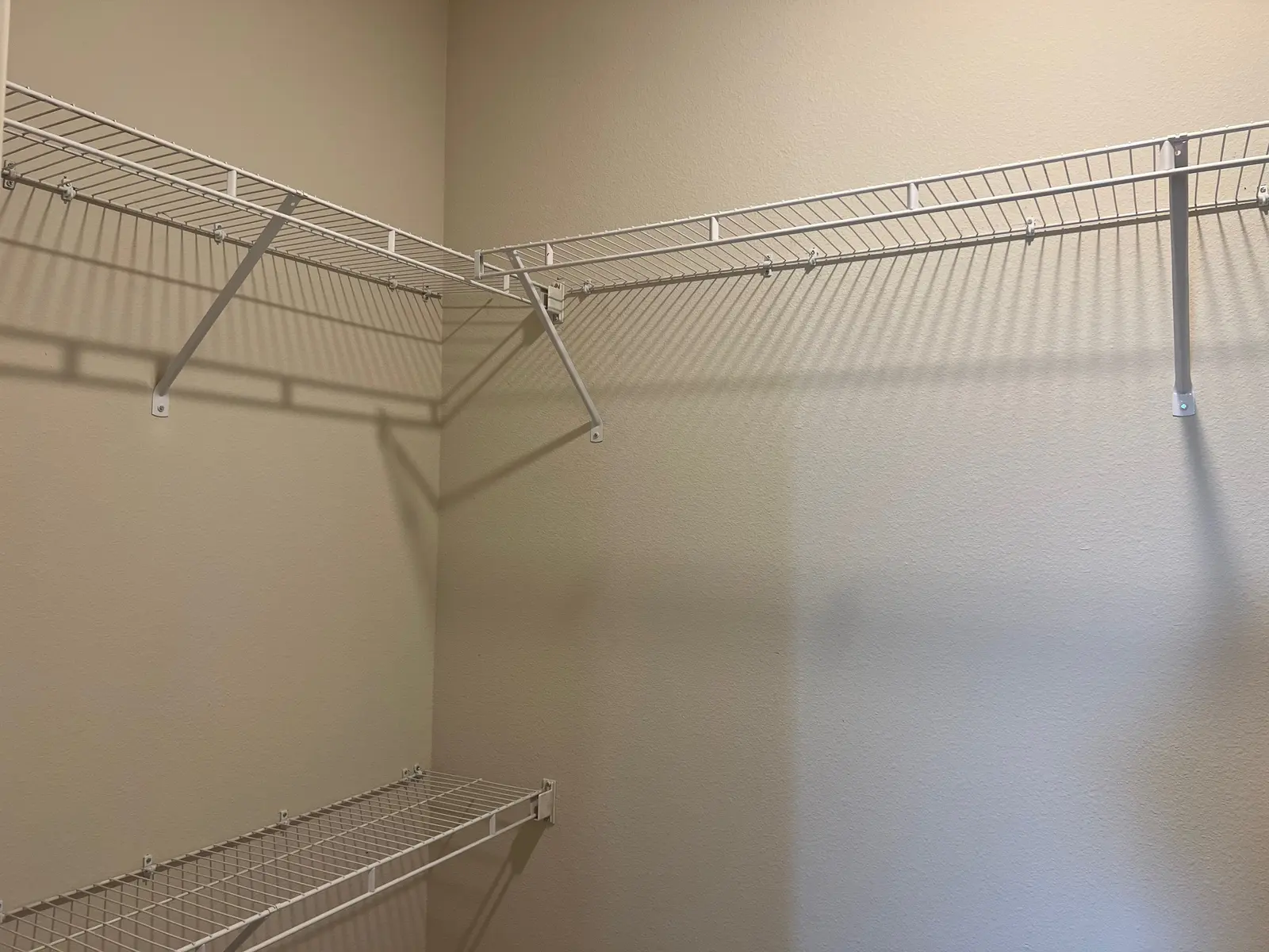 An empty closet with white wire shelves attached to the walls, set against a light beige background.